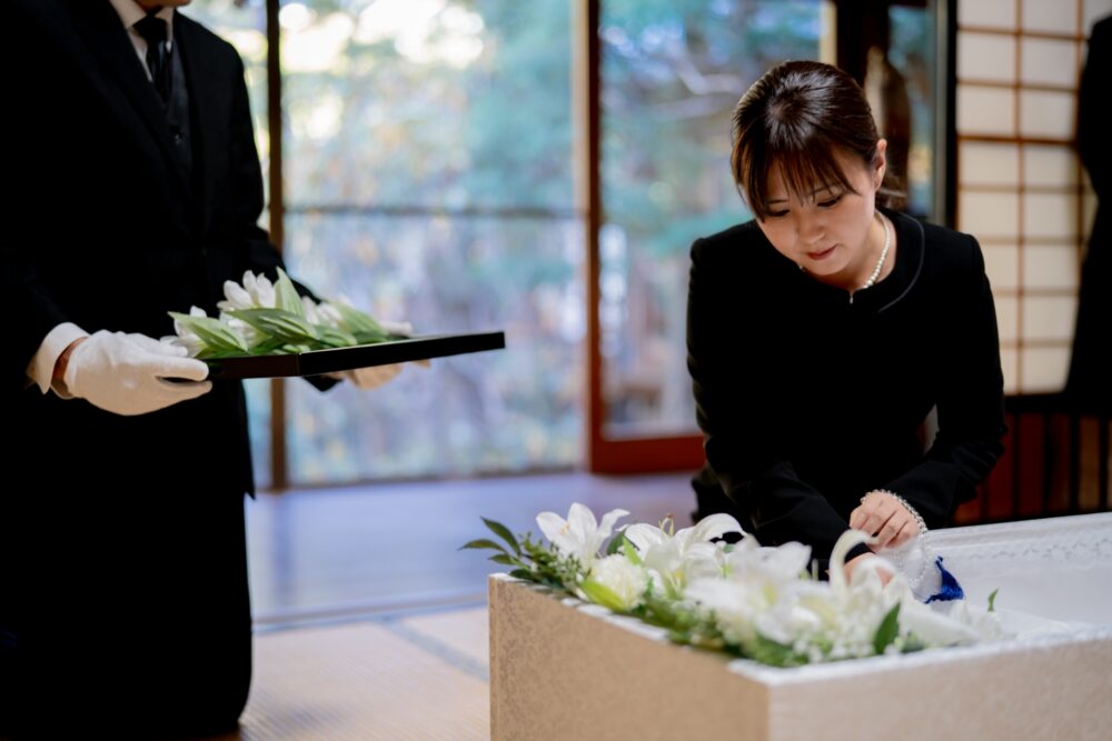 棺に花を手向ける女性の画像