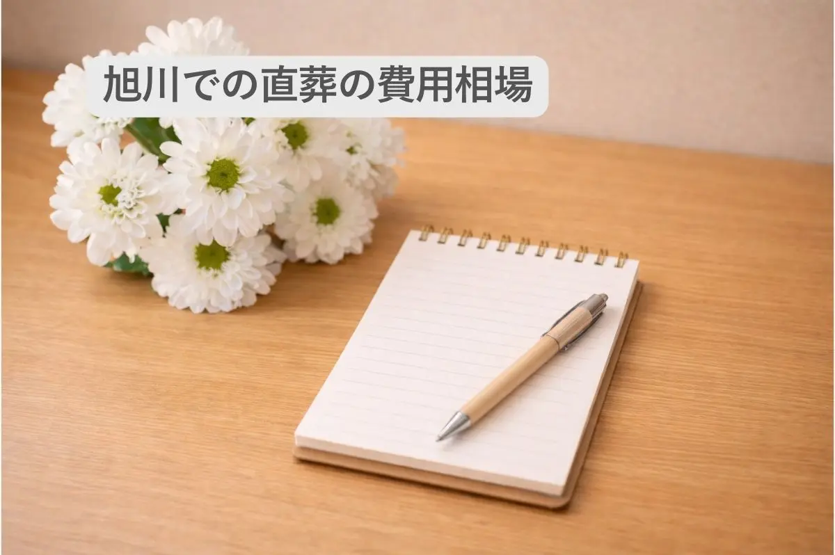 机の上におかれた菊の花とメモ帳の画像と「旭川での直葬の費用相場」の文字