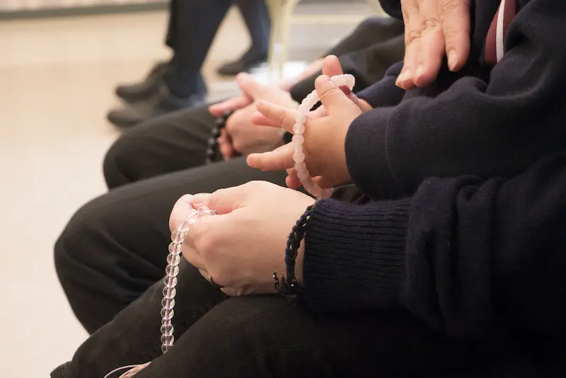 葬儀式場内で着席する参列者の、数珠をかけた手元の画像
